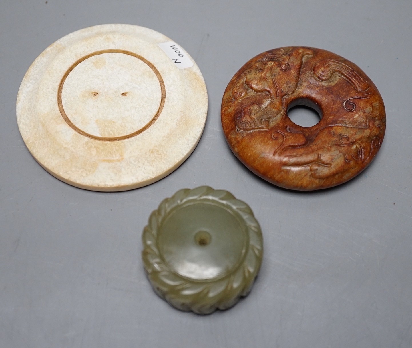 A Chinese green jade 'cash' pendant, a russet jade bi-disc and a burnt jade circular plaque